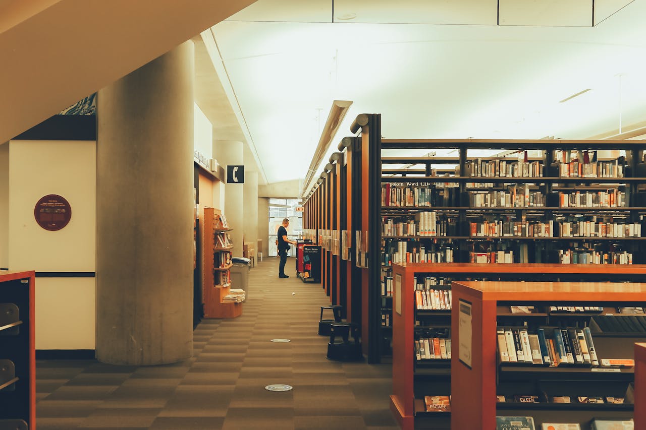 Wide-angle view of a modern library with extensive bookshelves and a solitary reader.